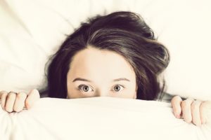 Ein Mädchen lugt unter der Bettdecke hervor