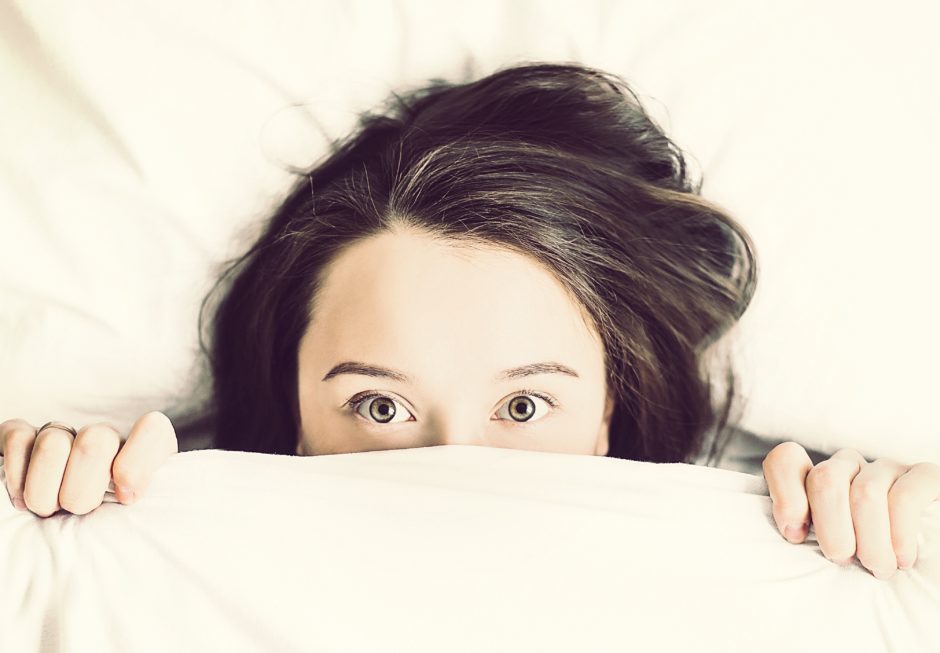 Ein Mädchen lugt unter der Bettdecke hervor