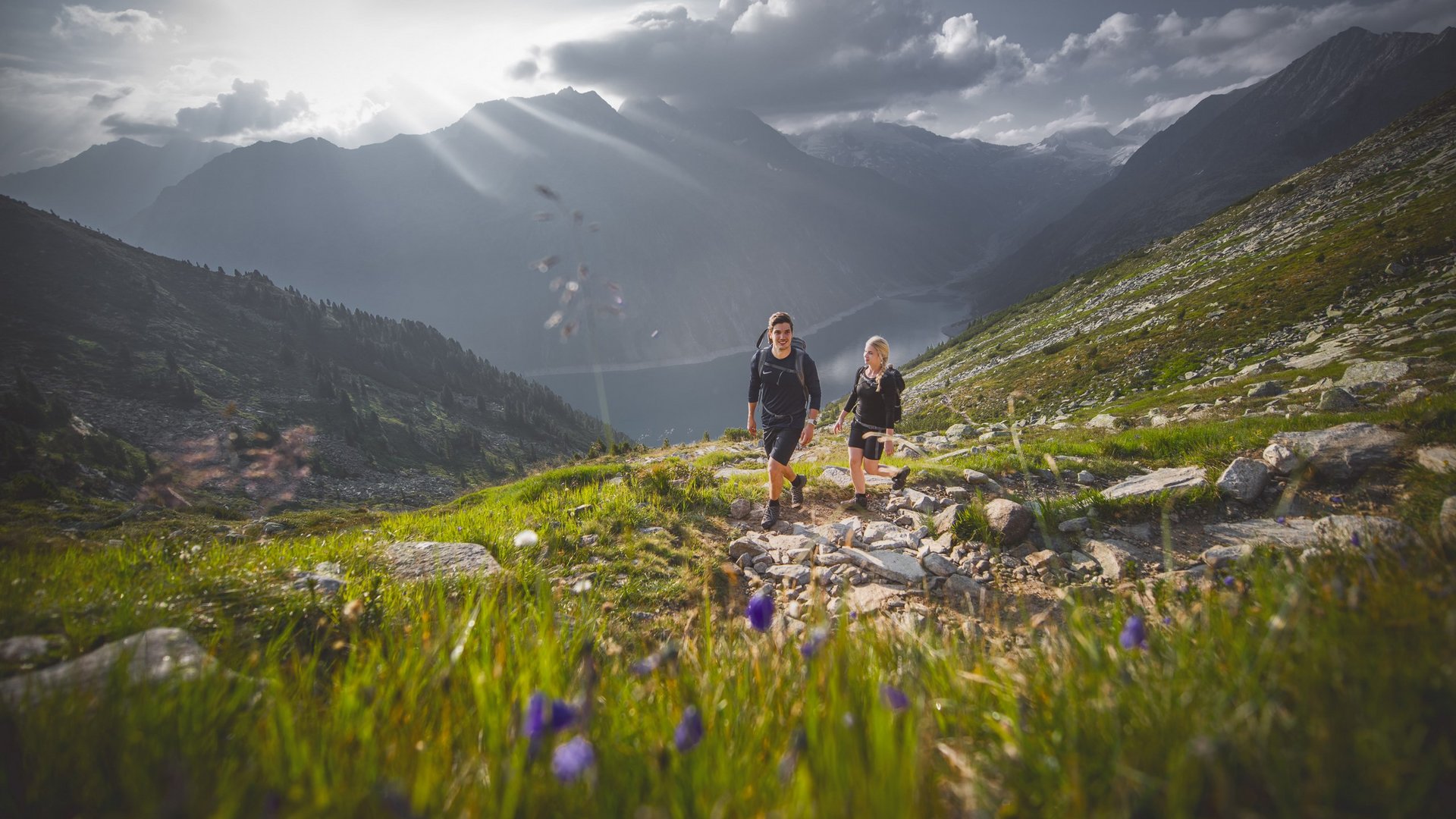 Sonnenaufgangswanderung Zwei Wanderer genießen einen sonnigen Morgenpfad in den Bergen mit weitem Talblick.