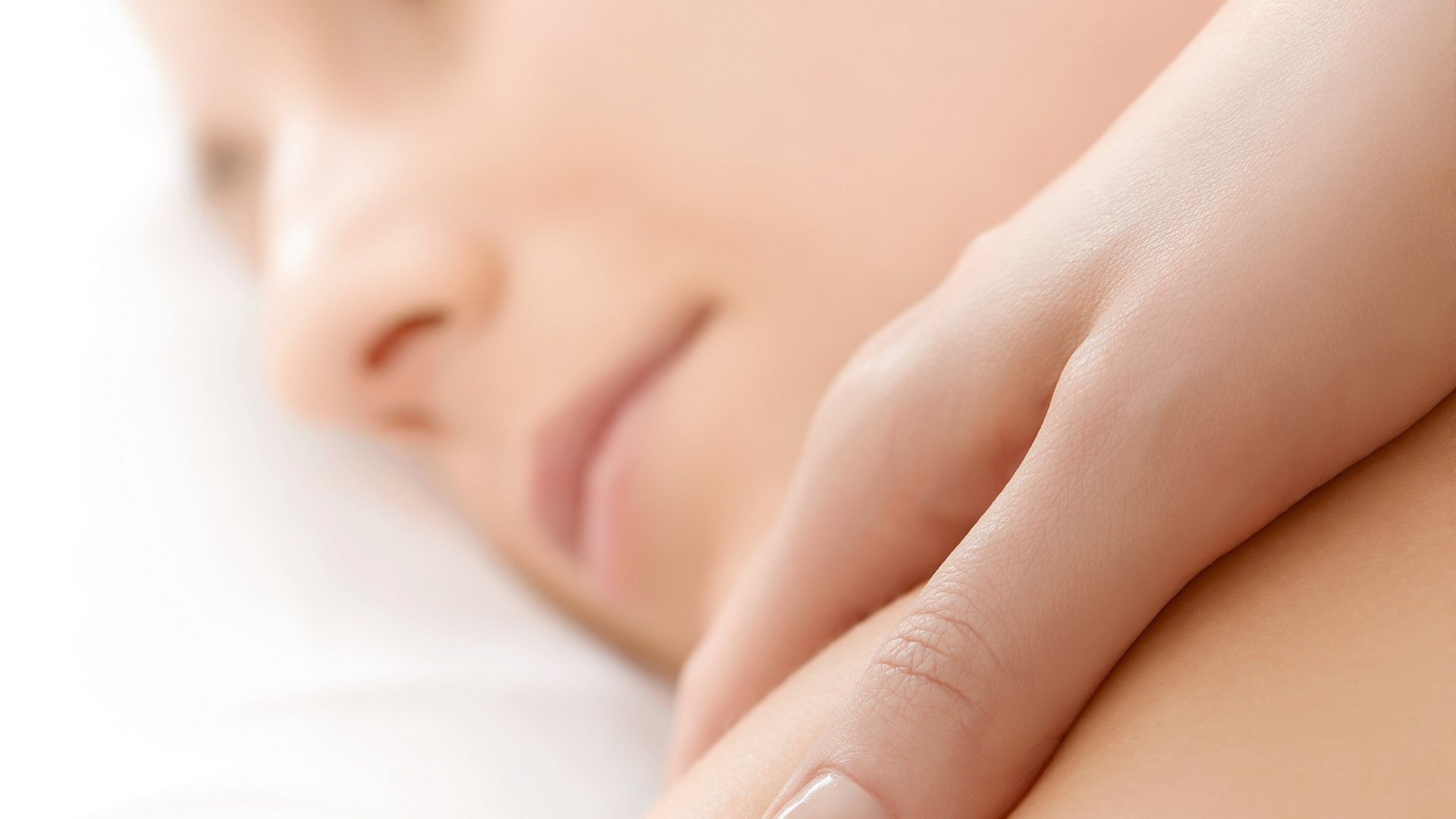 Person enjoys gentle massage on bare shoulder, eyes closed, relaxed atmosphere.
