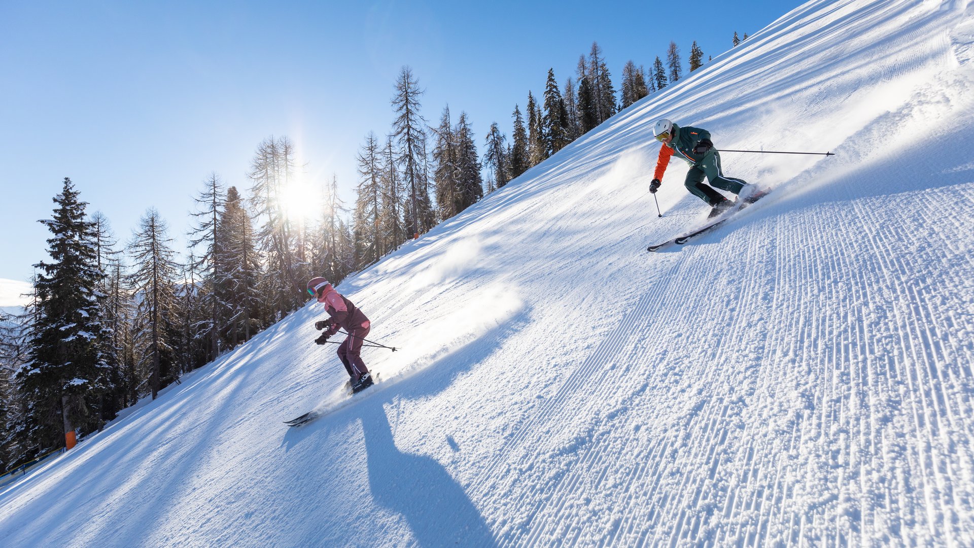 Skiing adventures in the sunshine Two skiers on a sunny slope, surrounded by snow-covered trees and a blue sky.